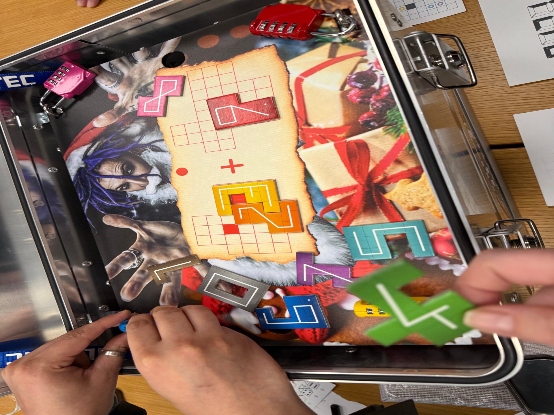 Hände am geöffneten Alukoffer mit weihnachtlichem Rätselbrett und farbigen Puzzleteilen